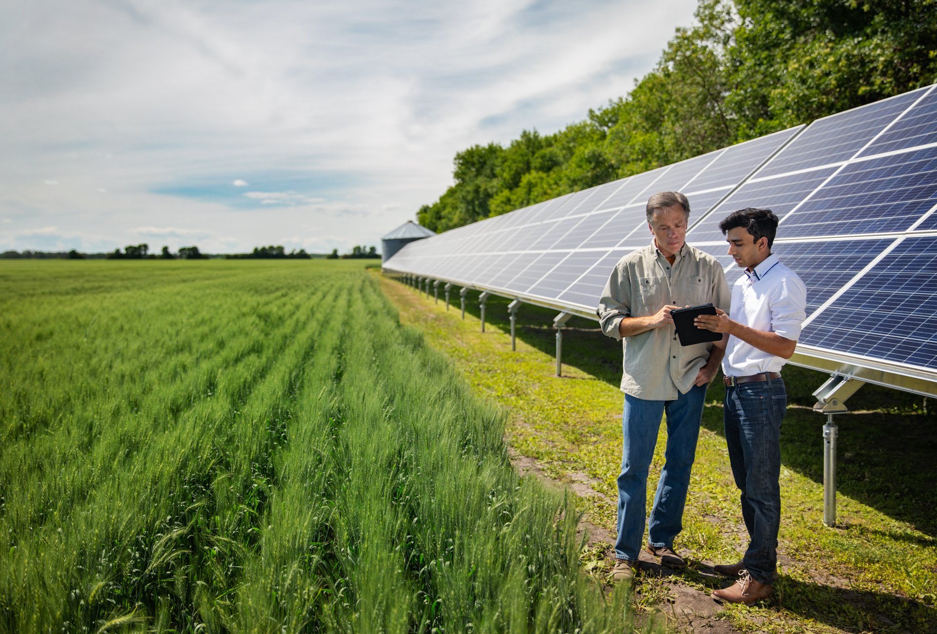 Two men stand before solar panels, symbolizing collaboration between farmers and manufacturers in sustainable energy.