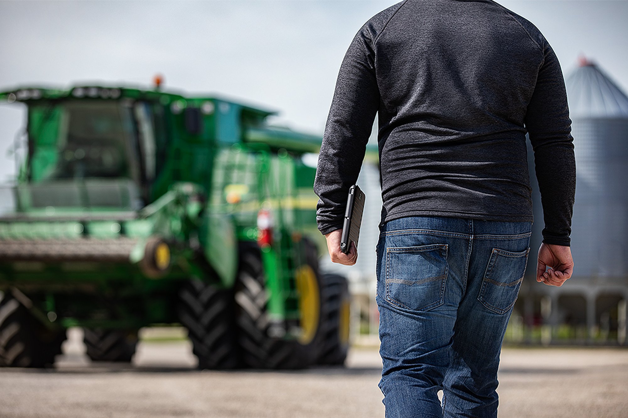 A man walks in front of a green tractor, engaged in agronomy operations in a rural landscape A man walks in front of a green tractor, engaged in agronomy operations in a rural landscape